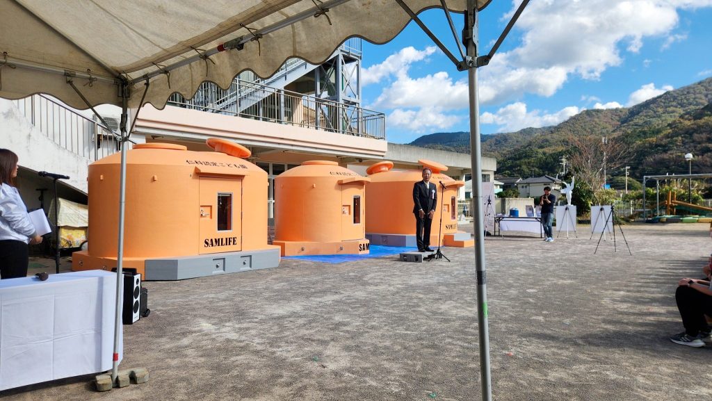 西伊豆町の仁科認定こども園にて開催された、株式会社小野田産業の津波シェルター『SAMLIFE』の除幕式の様子。高橋治教授や関係者が列席している。